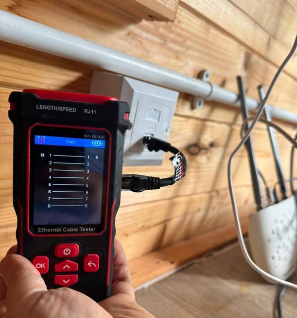 Engineer testing Cat6 ethernet cabling with a cable tester next to a router in a garden office