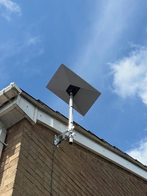 Starlink dish on a pole mount fixed to a residential brick wall under a clear sky