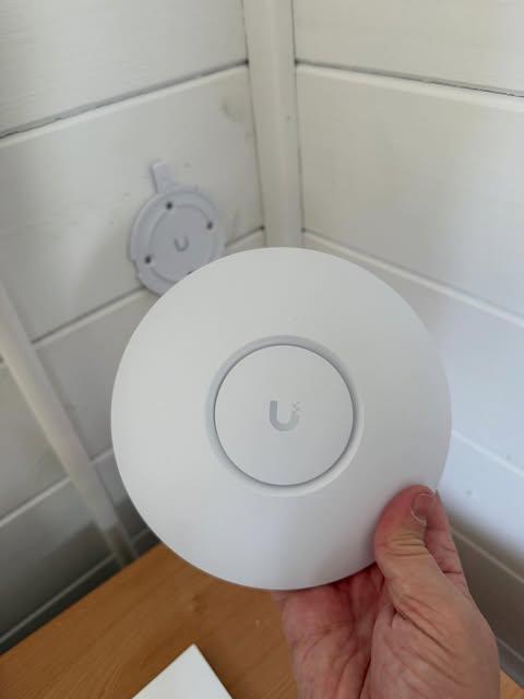 White Ubiquiti UniFi access point held up ready to mount on a garden office timber wall